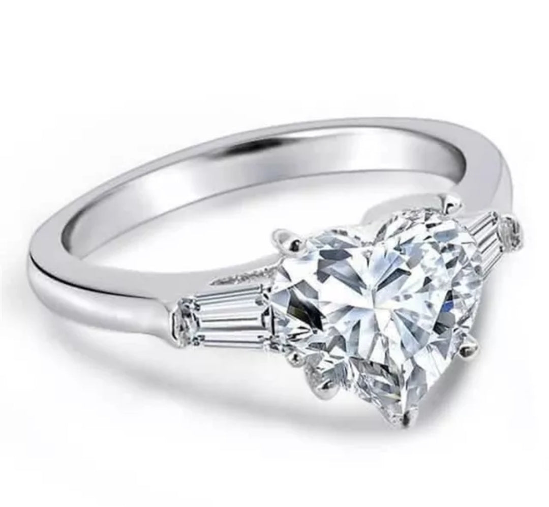 The DiamondVeneer Fashion 5CT Heart Cubic Zirconia Ring (635R71352) features a platinum-plated band with a large heart-shaped center stone and tapered baguette accents, displayed against a white background.