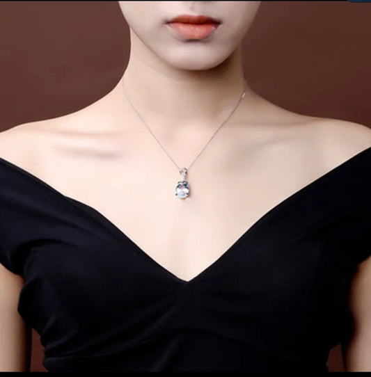 A woman in an off-the-shoulder black dress displays a Zirconmania Fashion Jewelry Blue Topaz Cubic Zirconia Pendant (Zirconite 851P351) against a brown background.