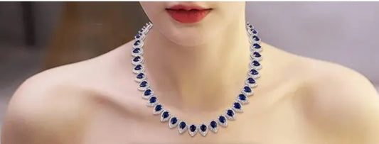 A woman showcases the zirconmania fashion jewelry Cubic Zirconia statement necklace, Zirconite, its sparkling blue teardrop pendants elegantly highlighting her bare shoulders and neck.