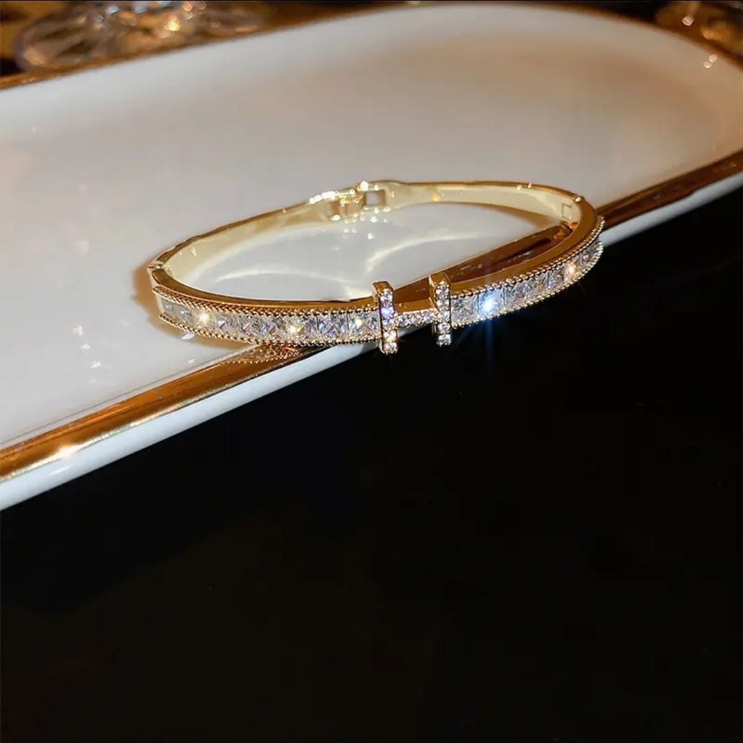 Nude-manicured hand displays Zirconmania gold CZ bangle bracelet with square channel set for a sparkling, unisex jewelry look.