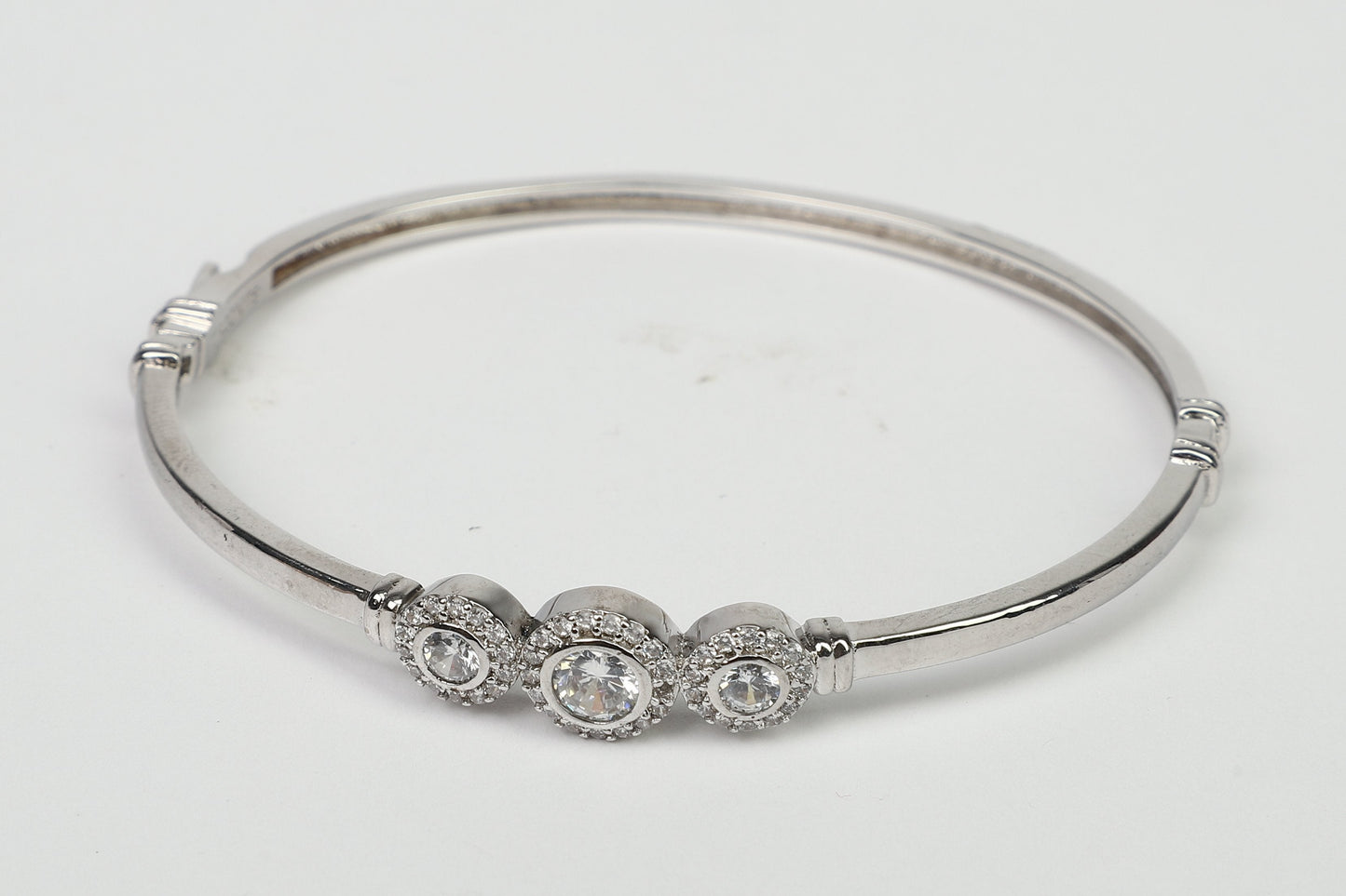 The DiamondVeneer Fashion Hinged Zirconite Cubic Zirconia 3-Stones Bezel Rhodium Bangle Bracelet.698B003, featuring three clear stones with sparkling accents, is showcased on a plain white background.