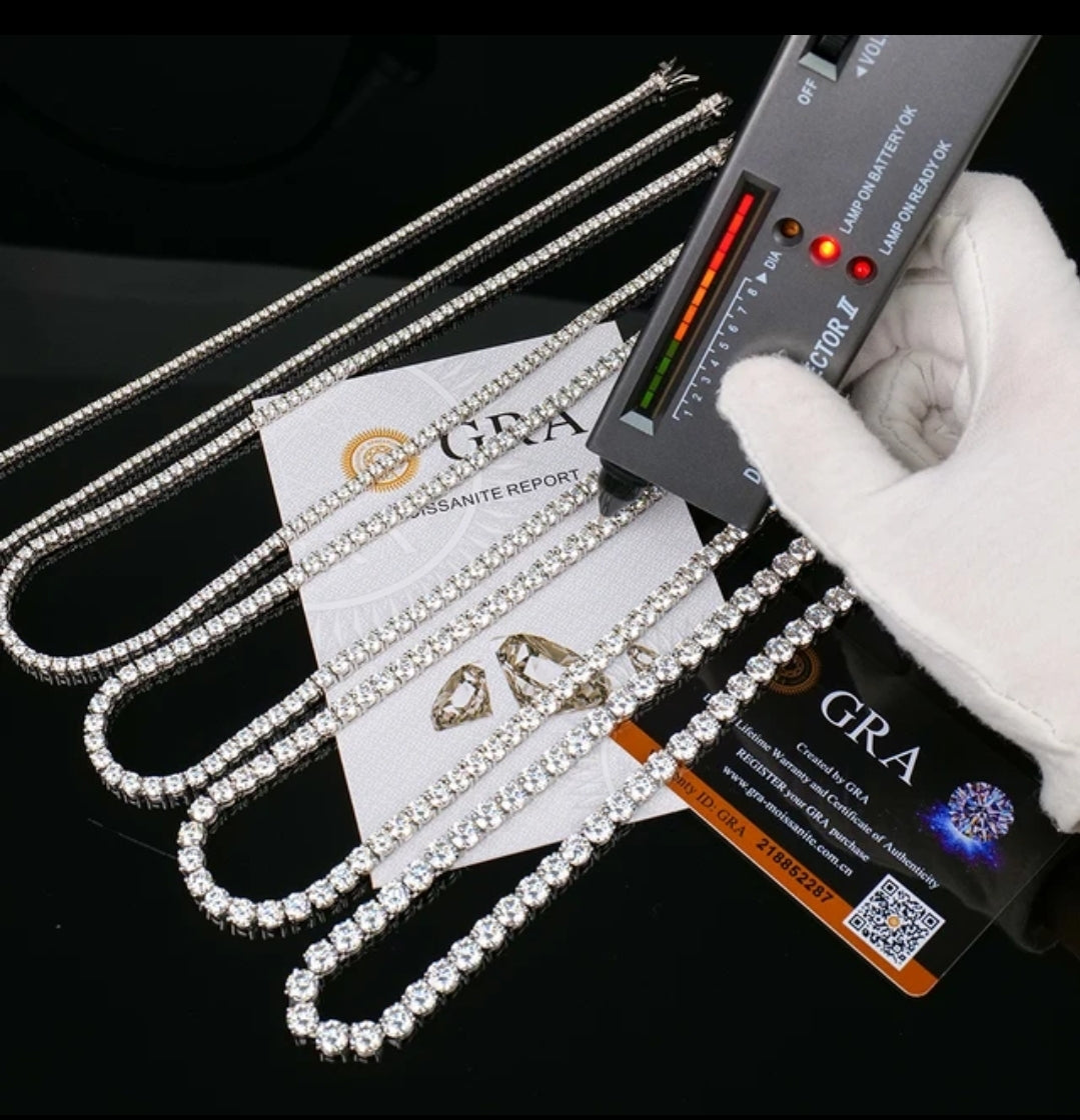 A gloved hand uses a diamond tester on the DiamondVeneer Fashion Moissanite Lab Created Diamond Tennis Necklace (850N4MM), shown with GRA certification, authenticity card, and other jewelry—an elegant diamond alternative on glossy black.