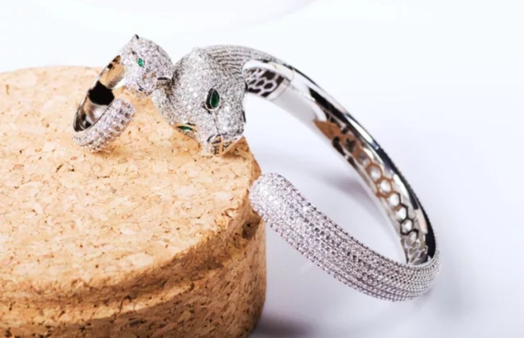 The DiamondVeneer Fashion Panther Zirconite Cubic Zirconia Hinged Bangle Bracelet 815B200 features a panther head with green gemstone eyes and sparkling stones, displayed on a cork surface against a white background.
