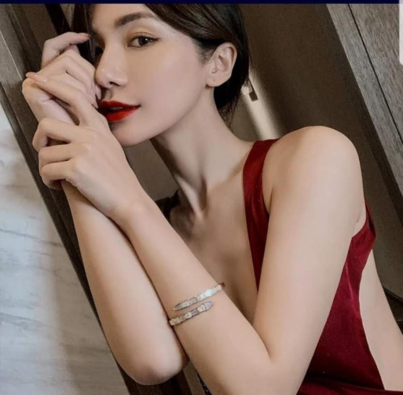 A woman in a sleeveless deep red dress, with red lipstick and straight dark hair, poses indoors wearing the DiamondVeneer Fashion Face-off natural Shell Stainless Steel Bangle Bracelet (709B12) on her wrist.