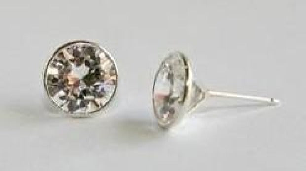A pair of Diamond Veneer jewelry Martini set Stud 14K Gold Earrings (635EPWIRE-K) with round, clear gemstones—one upright, one flat on a light surface.