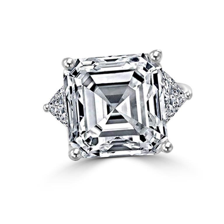 The DiamondVeneer Fashion Three Stones Asscher Cut Cubic Zirconia Engagement Ring (635R72192) features a large square-cut stone, geometric design, four-prong setting, and clusters of round stones on each side in white metal.