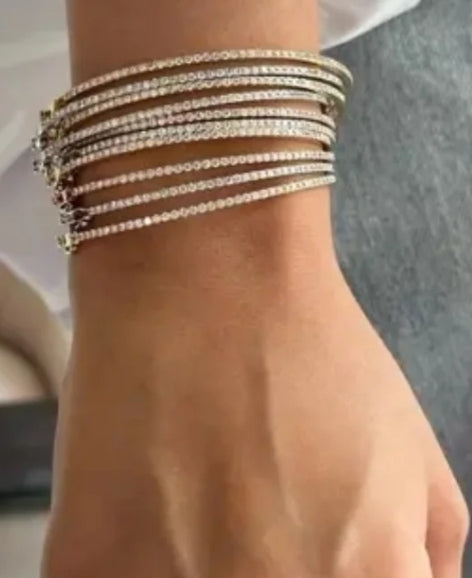 Close-up of a wrist adorned with stacked thin diamond bracelets, sparkling elegantly against a soft, blurred background for jewelry style.