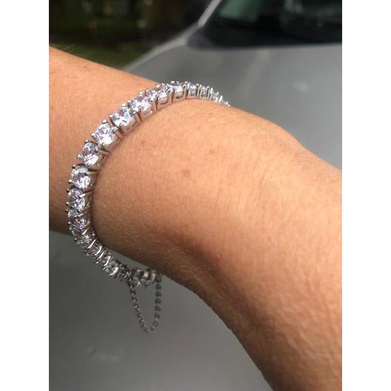 Sparkling silver bracelet with clear gemstones on wrist, close-up; blurred outdoor scene and gray car in background. Fashion jewelry detail.