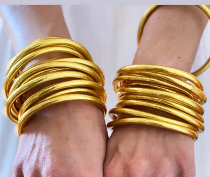 Close-up of two hands wearing multiple Zirconmania Fashion Jewelry Buddhist Gold Silicone Temple Bangle Bracelets (859B100G), showcasing their shiny 18k gold look against a light background.