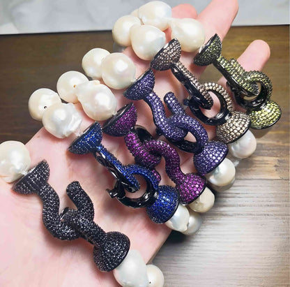 A hand displays five DiamondVeneer Fashion Baroque Fresh Water Pearls w/jeweled Zirconite Bracelets, showcasing large white pearls and jeweled clasps, elegantly arranged on a wooden surface—a must-have for pearl lovers.