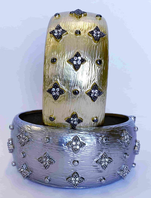 Two ornate cuff bracelets—one gold, one silver—with textured surfaces and raised diamond-shaped gemstone clusters. The designer-inspired gold cuff nests in the silver, resembling the DiamondVeneer Fashion Zirconite wide hinged Bangle Bracelet (500B7140).
