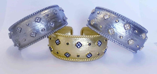 Three wide Zirconite hinged bangle bracelets by DiamondVeneer Fashion (500B7144)—two in silver, one in gold—feature a satin finish and sparkling crystal beaded floral designs.