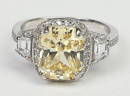 The DiamondVeneer Fashion 3.5CT Cushion Diamond Veneer Cubic Zirconia 14K Gold Ring (635R71567K) showcases a large rectangular yellow center stone, surrounded by clear stones and two square clear gems on each side.