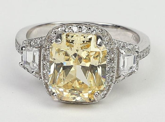 The DiamondVeneer Fashion 3.5CT Cushion Diamond Veneer Cubic Zirconia 14K Gold Ring (635R71567K) showcases a large rectangular yellow center stone, surrounded by clear stones and two square clear gems on each side.