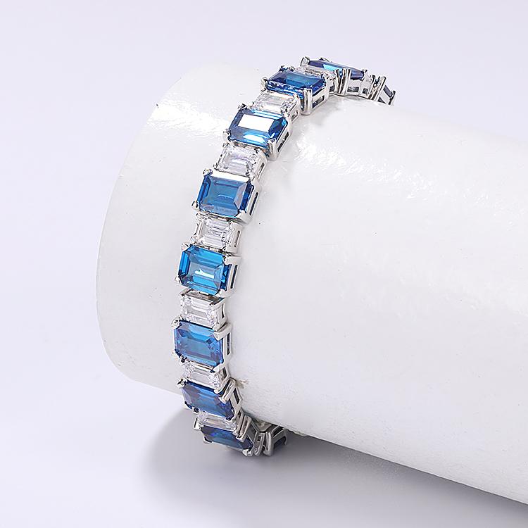 The DiamondVeneer Fashion Couture Emerald Cut Zirconite Cubic Zirconia Bracelet (809B1425) features rectangular blue gemstones in silver links, elegantly draped around a white cylindrical stand on a light background.