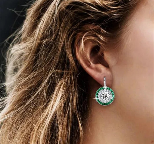 Close-up of a womans ear with wavy brown hair, wearing DiamondVeneer Fashion 4CT TW Diamond Veneer vintage Round Earrings (830E1045), featuring a large central diamond accent and green gem border.