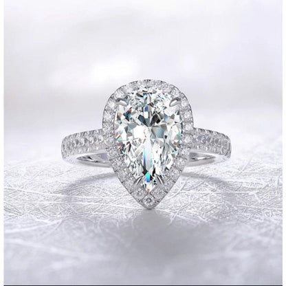 A close-up of the DiamondVeneer Fashion 4CT Pear Diamond Veneer Cubic Zirconia halo 14K Gold Ring (635R71421K), featuring a pear-shaped center stone, halo setting, and diamond-encrusted band against a soft background.