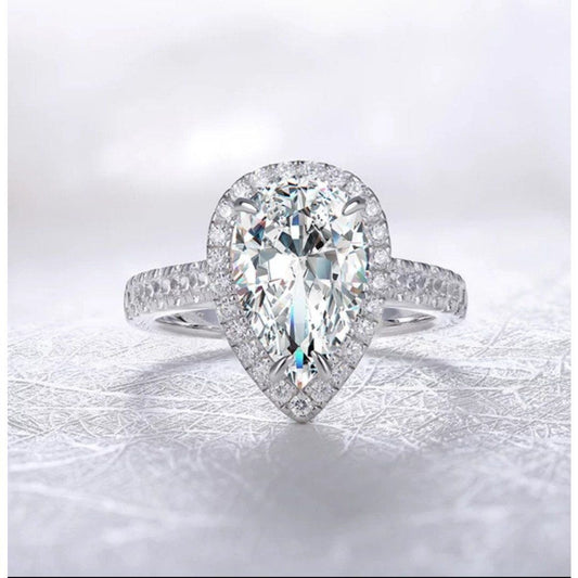 A close-up of the DiamondVeneer Fashion 4CT Pear Diamond Veneer Cubic Zirconia halo 14K Gold Ring (635R71421K), featuring a pear-shaped center stone, halo setting, and diamond-encrusted band against a soft background.