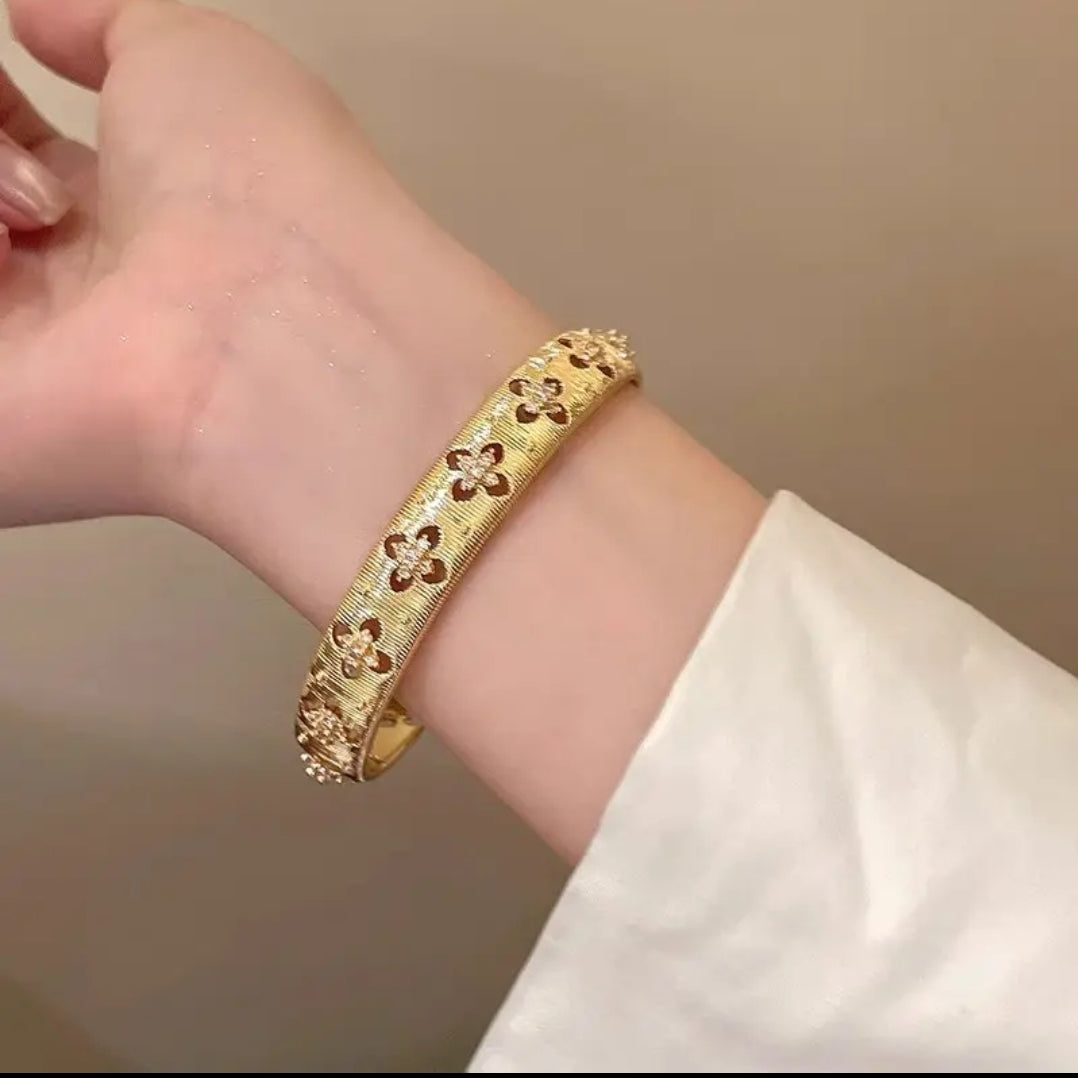 Hand models textured gold open cuff bangle by Zirconmania, featuring a star detail; elegant design on neutral beige background.