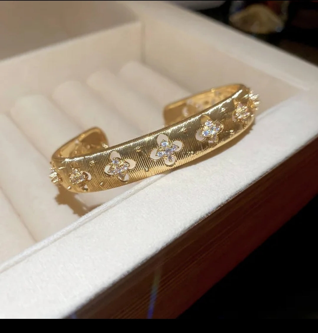 Hand models textured gold open cuff bangle by Zirconmania, featuring a star detail; elegant design on neutral beige background.