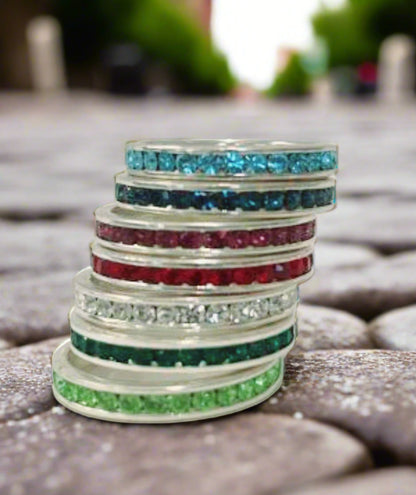 A stack of seven DiamondVeneer Fashion Ring Crystal eternity bands in vibrant gemstone colors—blue, dark blue, pink, red, clear, green, and light green—creates a lively twist on the minimalist luxe ring trend.