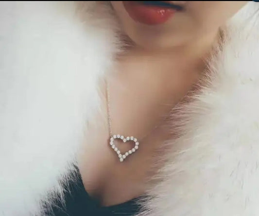 A person in a white fur garment wears a DiamondVeneer Fashion Cubic Zirconia Heart Pendant (Zirconite.851P117), with red lipstick and the heart-shaped necklace resting on their chest.