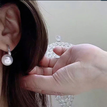 A close-up shows a person’s ear wearing DiamondVeneer Fashion White Pearls Cubic Zirconia Huggies Earrings (Zirconite, 851E2949), as their hand rests on their head, with a decorative transparent object in the background.