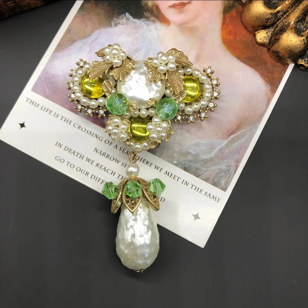Decorative brooch with Baroque pearls, yellow and green gemstones on a white background