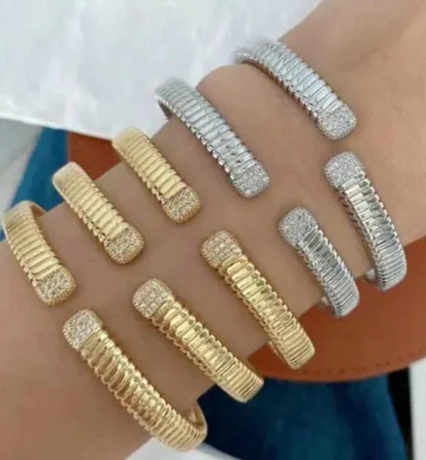 A close-up of a forearm wearing DiamondVeneer Fashions Designer Face-Off Bangle and Zirconite Bracelet (848B100), featuring five gold-tone and three silver-tone textured styles with sparkling gem-encrusted ends against a blurred background.