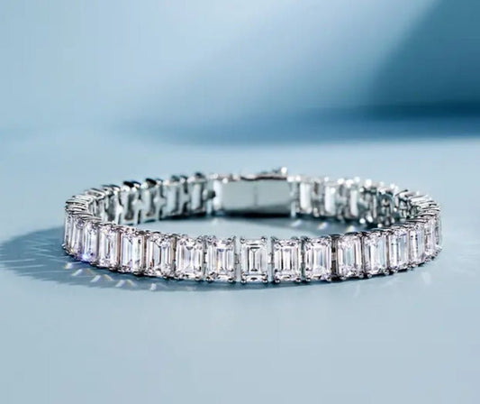 The DiamondVeneer Fashion Emerald cut Zirconite Cubic Zirconia Bracelet (602B30169) features rectangular stones set in a luxe silver or white gold band, shown on a light blue surface with a gradient background for intense shine.