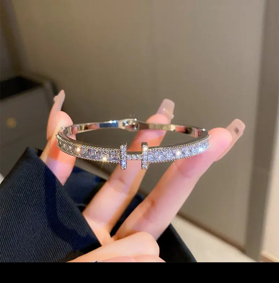 Nude-manicured hand displays Zirconmania gold CZ bangle bracelet with square channel set for a sparkling, unisex jewelry look.