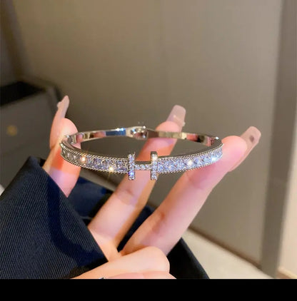 Nude-manicured hand displays Zirconmania gold CZ bangle bracelet with square channel set for a sparkling, unisex jewelry look.