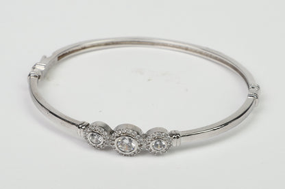 The DiamondVeneer Fashion Hinged Zirconite Cubic Zirconia 3-Stones Bezel Rhodium Bangle Bracelet.698B003, featuring three clear stones with sparkling accents, is showcased on a plain white background.