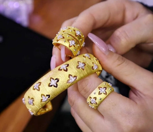 A person holds the DiamondVeneer Fashion Inspired Italian design satin open Bangle (831B104) with gold rings, all featuring star-shaped cutouts, small diamonds, and textured finishes. Their nails are long and manicured.