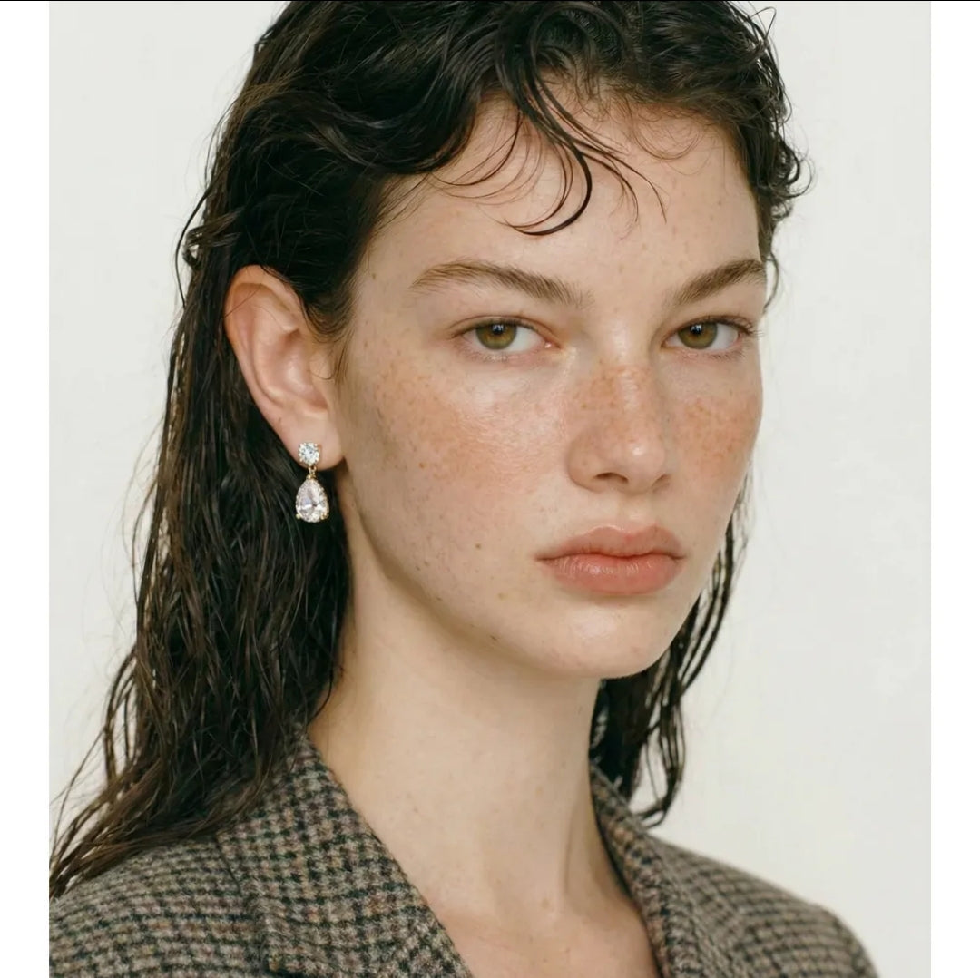 Woman with wet wavy hair in plaid blazer models Zirconmania pear drop cubic zirconia earrings against plain light background.