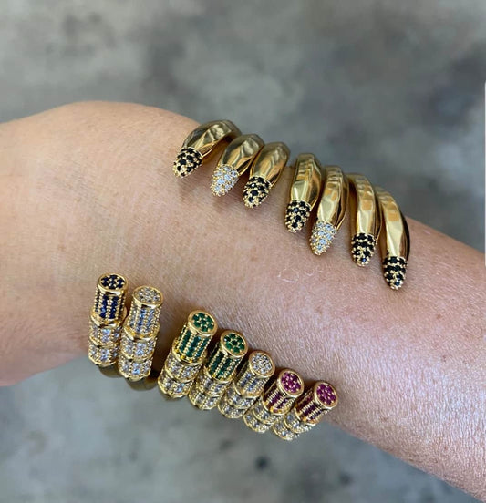 A wrist featuring two gold bracelets: a serpent-head with black and clear stones, and the DiamondVeneer Fashion Pencil Bangle Bracelet Cuff Zirconite Cubic Zirconia 843B100—an adjustable, colorful teacher gift.