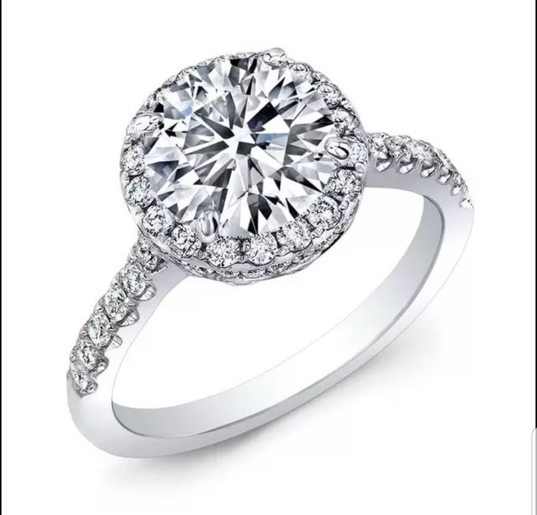 The DiamondVeneer Fashion Round Cubic Zirconia Halo Engagement Ring (800R70/2) features a striking center stone, haloed by smaller gems and accented with extra stones along the white gold band for added brilliance.
