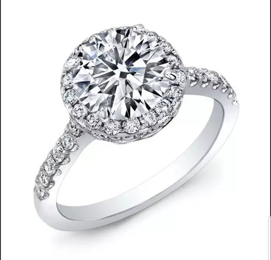 The DiamondVeneer Fashion Round Cubic Zirconia Halo Engagement Ring (800R70/2) features a striking center stone, haloed by smaller gems and accented with extra stones along the white gold band for added brilliance.