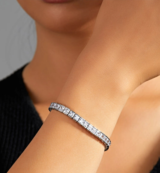 A close-up of a wrist wearing the zirconmania Fashion Jewelry Square Cubic Zirconia Tennis Bracelet (Zirconite 602B30017) with square-cut stones, set against a neutral background. The wearer is dressed in a black top.