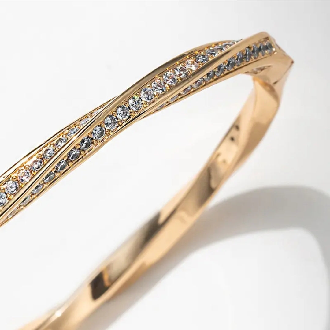 The Twisted Gold Pavé CZ Bangle Bracelet by Zirconmania Fashion Jewelery features two parallel rows of sparkling CZ and a unique twisted design, making it a striking unisex luxury accessory for any occasion.