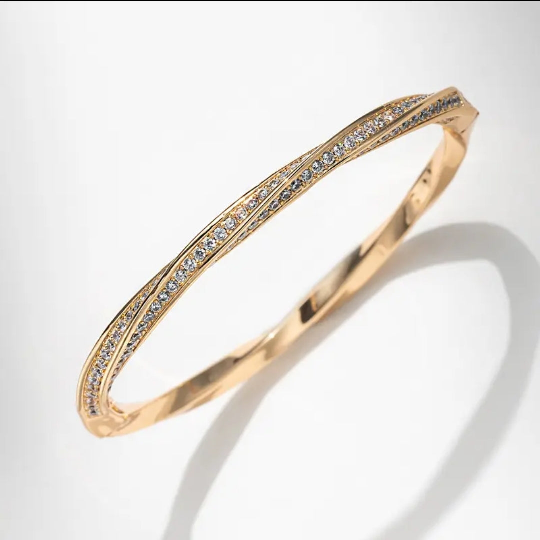 The Twisted Gold Pavé CZ Bangle Bracelet by Zirconmania Fashion Jewelery features two parallel rows of sparkling CZ and a unique twisted design, making it a striking unisex luxury accessory for any occasion.