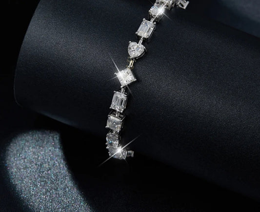 The DiamondVeneer Fashion Zirconite Multi Shaped Cubic Zirconia Bracelet (854B100) shines brilliantly on a black textured surface, its varied shapes reflecting light for a sparkling effect.