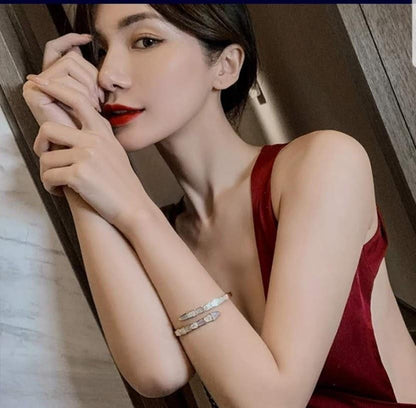 A woman in a sleeveless deep red dress, with red lipstick and straight dark hair, poses indoors wearing the DiamondVeneer Fashion Face-off natural Shell Stainless Steel Bangle Bracelet (709B12) on her wrist.