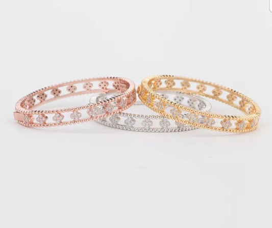 Three ornate Clover stations Zirconite Cubic Zirconia Bangle Bracelets by DiamondVeneer Fashion in rose gold, silver, and gold are overlapped on a white background, each with a beaded edge and intricate lattice design.