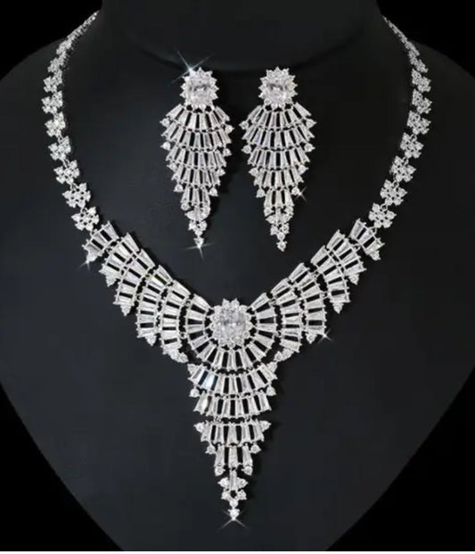 The DiamondVeneer Fashion Cubic Zirconia Buggetts Necklace Set final Sale.712N9103 features hand-set baguettes, geometric patterns, and a rhodium finish, displayed on black with matching dangling earrings.