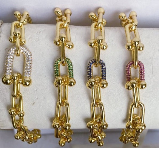 Four DiamondVeneer Fashion Zirconite Sadle stainless steel bracelets (821B100) are displayed on a white cylinder, each featuring a colored pavé center link in white, green, blue, or pink.