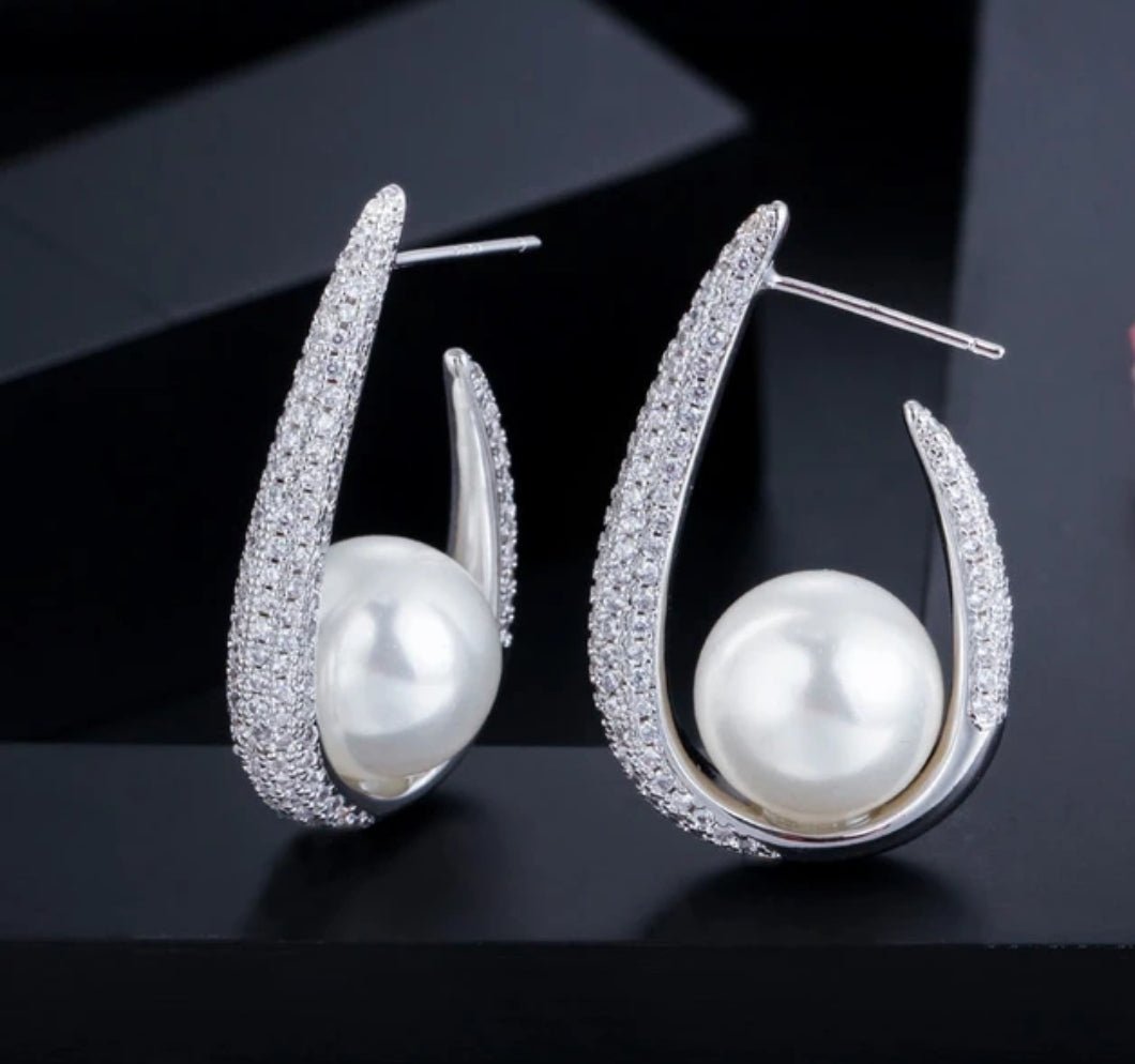 DiamondVeneer Fashion’s Zirconite Cubic Zirconia & Pearl Hoop Earrings (826E09) feature large round pearls set in curved, CZ-studded hoops, beautifully showcased against a dark background.