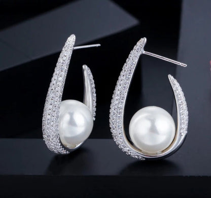 DiamondVeneer Fashion’s Zirconite Cubic Zirconia & Pearl Hoop Earrings (826E09) feature large round pearls set in curved, CZ-studded hoops, beautifully showcased against a dark background.