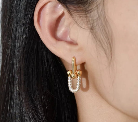 Close-up of a woman’s ear wearing DiamondVeneer Fashion Saddle Earrings Zirconite Cubic Zirconia (.821E100), featuring a gold and silver U-shaped hoop design that shines through her straight, dark hair.