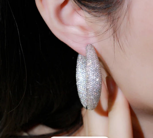 A close-up of a person’s ear wearing DiamondVeneer Fashion’s Zirconite Cubic Zirconia double view Hoop Earrings 826E04, encrusted with sparkling stones, as they gently touch their earlobe.